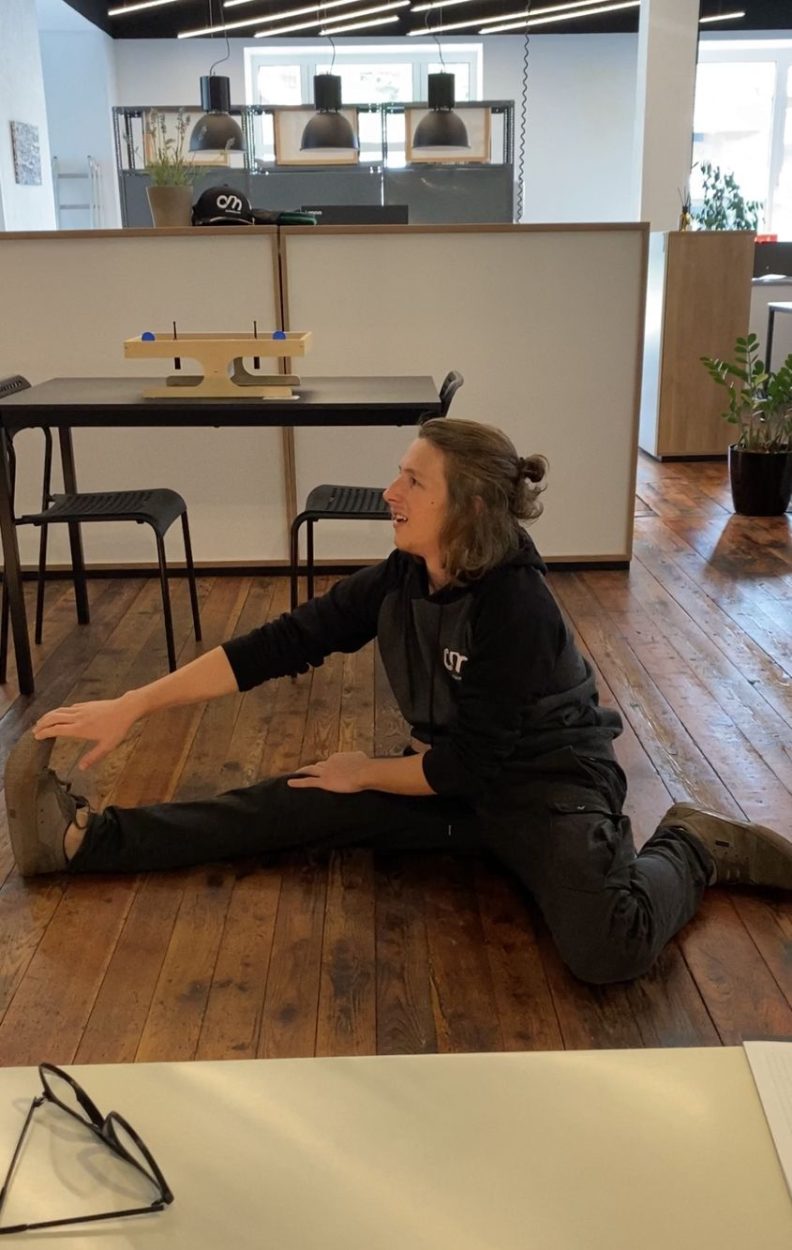 Elias macht eine Yoga Übung auf dem Boden im clubdrei Büro und lacht dabei