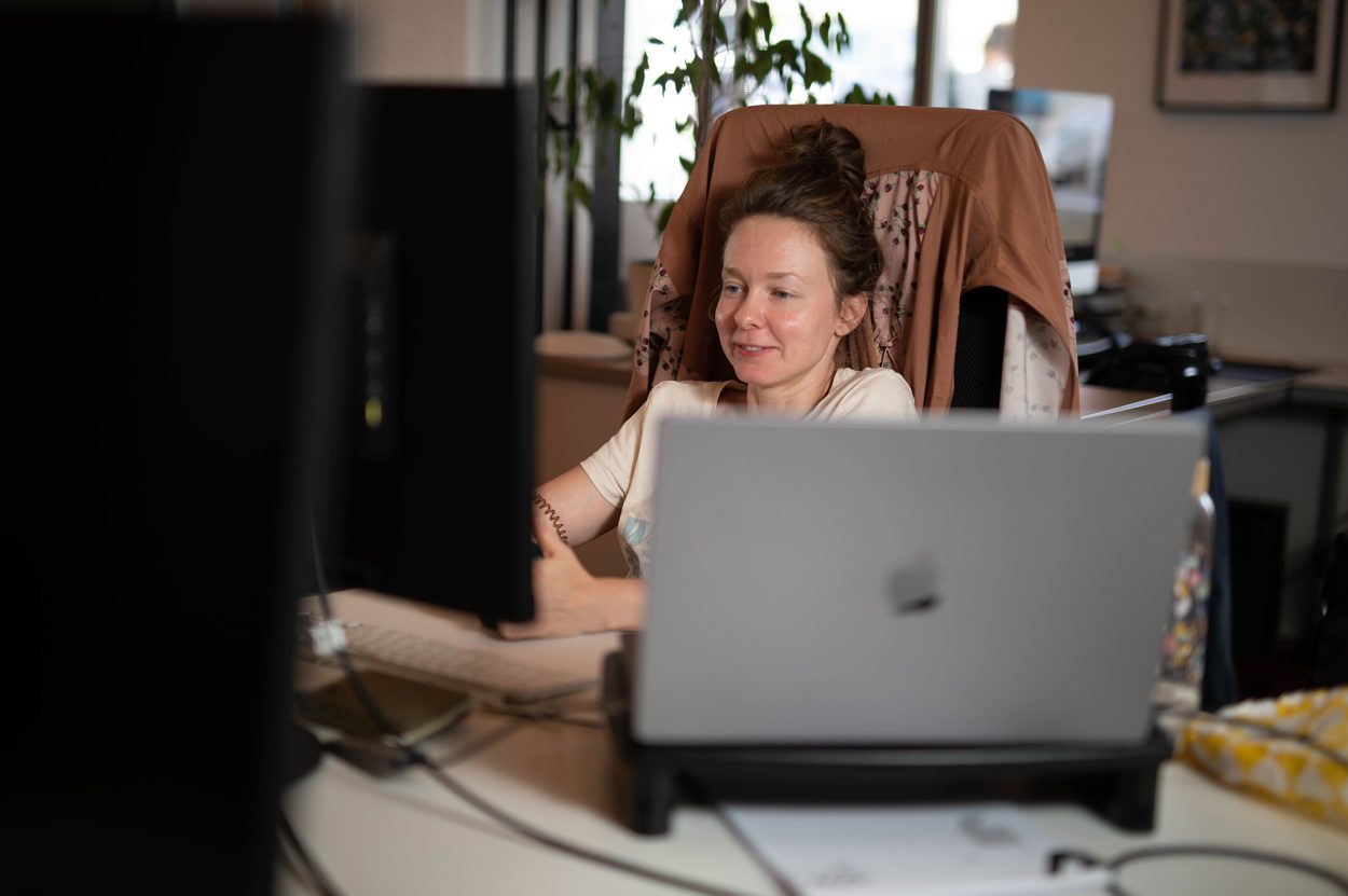 Anna arbeitet am Computer, sitzt entspannt auf ihrem Bürostuhl und lacht