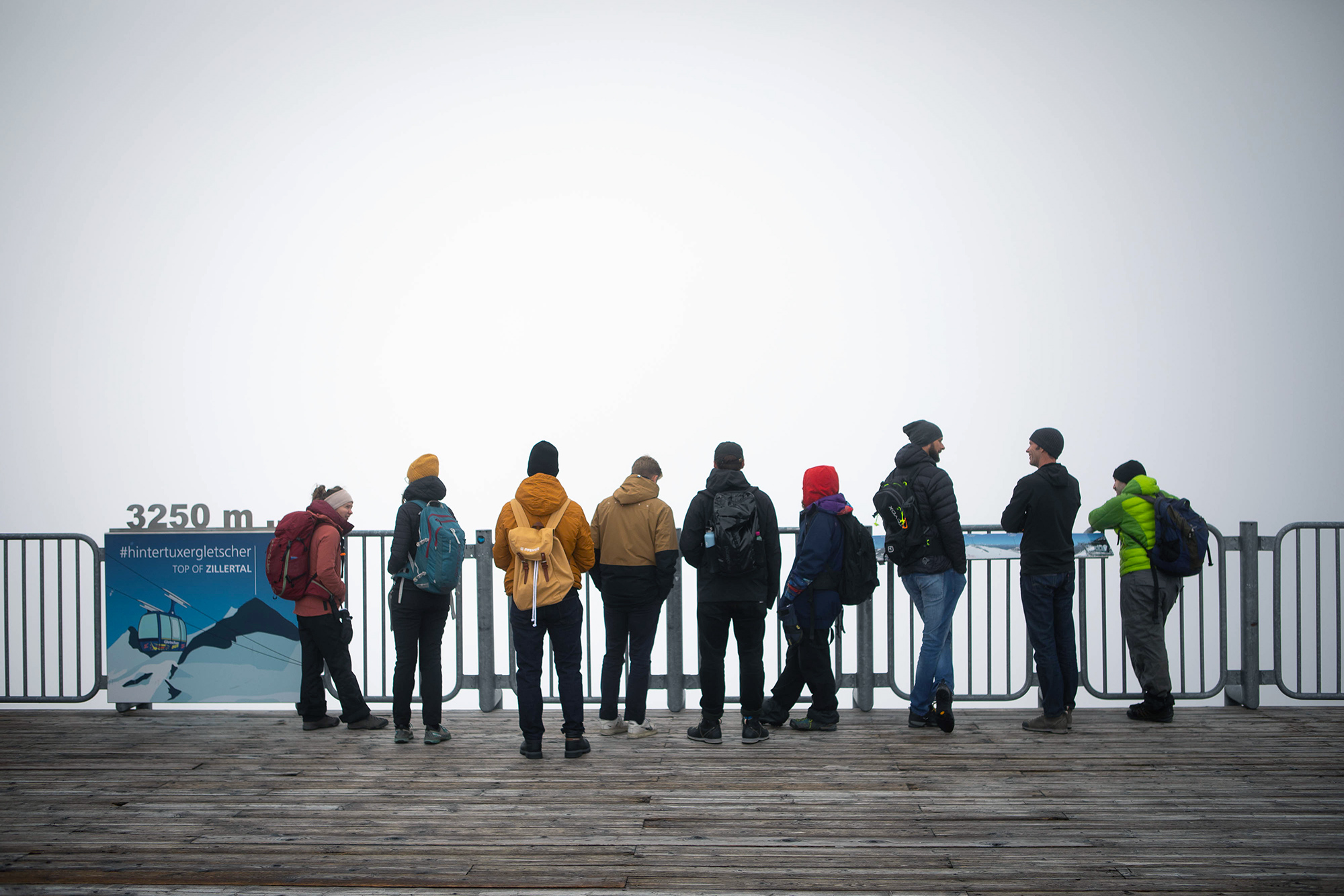 Eine Gruppe Menschen, die man von hinten sieht, steht in Winterkleidung an einem Geländer